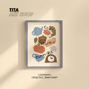 Puede incluir: Una impresión artística enmarcada con un marco azul claro. La obra de arte presenta ilustraciones coloridas de objetos con temática otoñal, incluyendo una tetera, una bellota y una calabaza. Las palabras "Cozy Autumn Essentials" están escritas en la impresión. El nombre de la tienda "TITA ART SHOP" está en la parte superior.