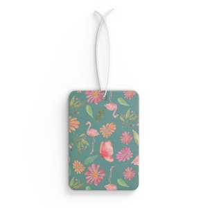 May include: Rectangular air freshener with a teal background featuring a pattern of pink flamingos, flowers, and green leaves. A white string is attached at the top for hanging. The design has a watercolor style.