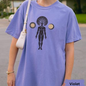 Könnte beinhalten: Ein violettes T-Shirt mit einem grafischen Aufdruck einer menschlichen Figur, aus deren Kopf ein Baum wächst. Die Grafik enthält auch eine Sonne und einen Mond.
