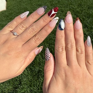 May include: Close-up of hands with almond-shaped nails painted with different patterns. The nails are painted with white polka dots, black and white polka dots, red and white abstract design, black and white animal print, and a blue and silver glitter design.
