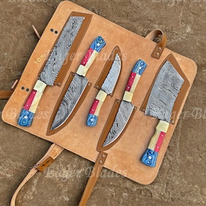 May include: A set of six knives with patterned blades and handles featuring red, white, and blue accents, displayed on a tan leather knife roll. The blades have a unique, textured design.