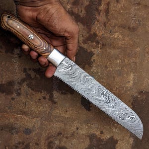 May include: A Damascus steel bread knife with a wooden handle. The blade has a wavy pattern, and the handle is a light brown color with a silver bolster. The knife is held in a hand.