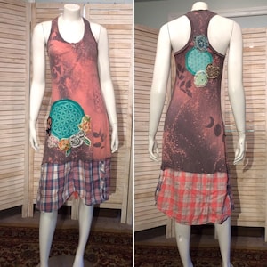 May include: A pink and brown sleeveless dress with a plaid skirt. The dress features a flower and geometric design on the front and a flower design on the back.