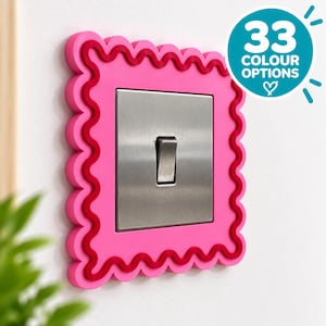 May include: A square light switch cover featuring a bright pink scalloped frame with a dark red wavy border detail. The center of the cover is a brushed silver metal plate with a single vertical toggle switch. A circular graphic states 33 COLOUR OPTIONS.