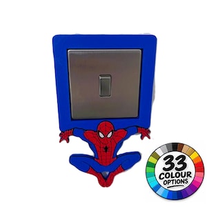 Op de afbeelding: Een blauwe vierkante lichtschakelaarafdekking met een rode en blauwe Spider-Man-figuur aan de onderkant. De schakelplaat is van metaalzilver met een centrale tuimelschakelaar. Een cirkelvormige afbeelding toont de tekst 33 COLOUR OPTIONS.