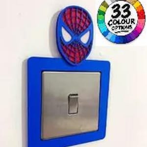 May include: A blue light switch cover plate featuring a red and blue Spider-Man mask emblem at the top. The centre of the plate is a metallic silver toggle switch. A circular graphic in the corner displays 33 colour options in a rainbow wheel.