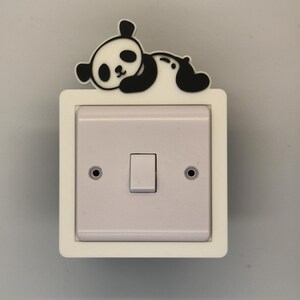 Op de afbeelding: Een witte lichtschakelaar met een zwart-witte panda sticker erop. De panda ligt met zijn kop op de schakelaar.