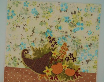 May include: A brown cornucopia filled with fall-themed decorations, including orange pumpkins, yellow flowers, and brown leaves. The cornucopia is on a background of a light brown fabric with a white floral pattern.