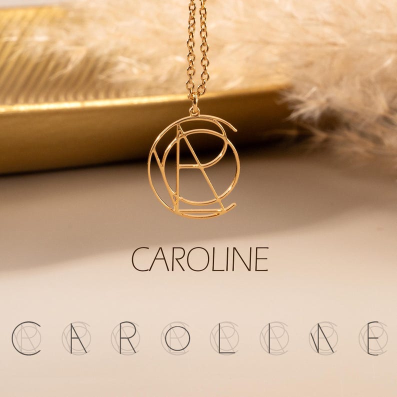 May include: Gold necklace with a geometric pendant featuring the letters "CAROLINE" in a circular design. The pendant is shown on a gold surface with the word "CAROLINE" written below it.