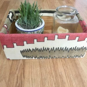 May include: A rectangular storage box with a red, white, and brown patterned fabric exterior. The box contains a potted plant and a glass jar with a candle inside.