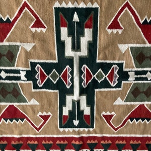 May include: Close-up of a woven textile with a geometric pattern. The design features repeating shapes in shades of tan, green, red, and white. The textile has a textured appearance, suggesting a natural fiber material.