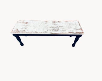 May include: A whitewashed wooden bench with black legs. The bench has a distressed finish and is perfect for adding a rustic touch to any room.
