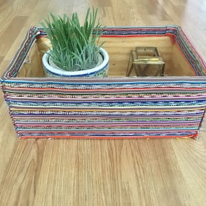 May include: A wooden box with a colorful striped fabric lining. The box contains a small potted plant and a gold candle holder.