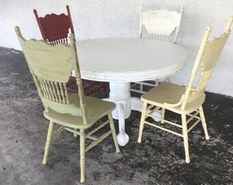 May include: A white round table with four chairs. Two chairs are painted a light green, one is painted white, and one is painted red.
