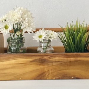 May include: A wooden tool caddy with three compartments, each holding a glass jar with white flowers and a potted green plant.