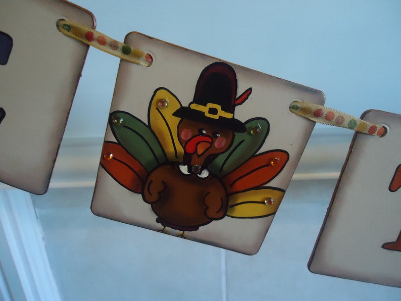 May include: A Thanksgiving banner with a painted turkey wearing a pilgrim hat. The turkey is brown with red, yellow, green, and orange feathers. The banner is made of wood and has a brown background.