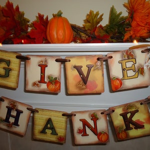 May include: A Thanksgiving banner with the words "Give Thanks" in brown letters on a cream background. Each letter is on a separate square with fall-themed designs and a small pumpkin.