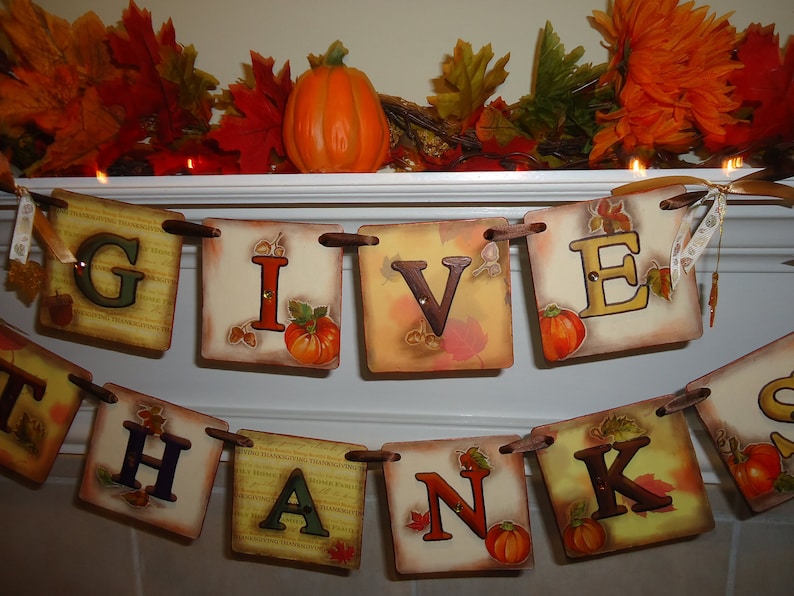 May include: A Thanksgiving banner with the words "Give Thanks" in brown letters on a cream background. Each letter is on a separate square with fall-themed designs and a small pumpkin.