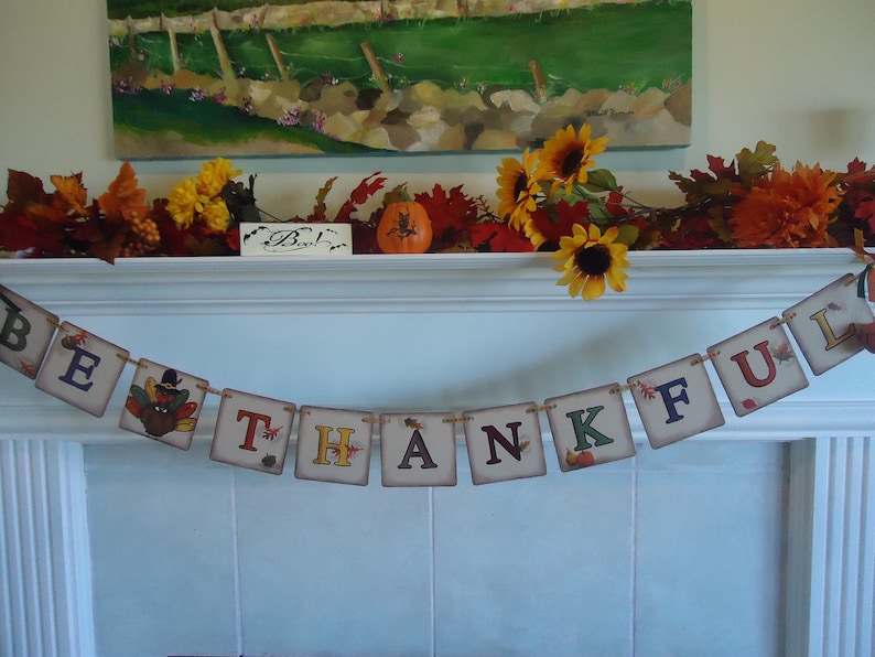 May include: A Thanksgiving banner with the word "BE THANKFUL" in colorful letters on a white background. The banner is decorated with fall leaves, pumpkins, and a turkey.