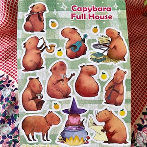 Peut inclure: Un ensemble de 10 autocollants représentant des capybaras dans diverses activités, notamment en train de jouer d'instruments de musique, de boire des cocktails et de lire des livres. Les autocollants sont sur un fond à carreaux vert et blanc avec des accents de fruits d'agrumes orange. Le texte "Capybara Full House" est en haut de la feuille.