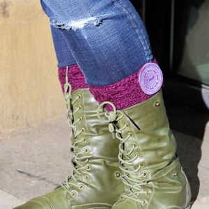 Puede incluir: Botas de combate de cuero verde con cordones y un pu&ntilde;o de punto morado. El pu&ntilde;o tiene un emblema redondo morado y plateado.