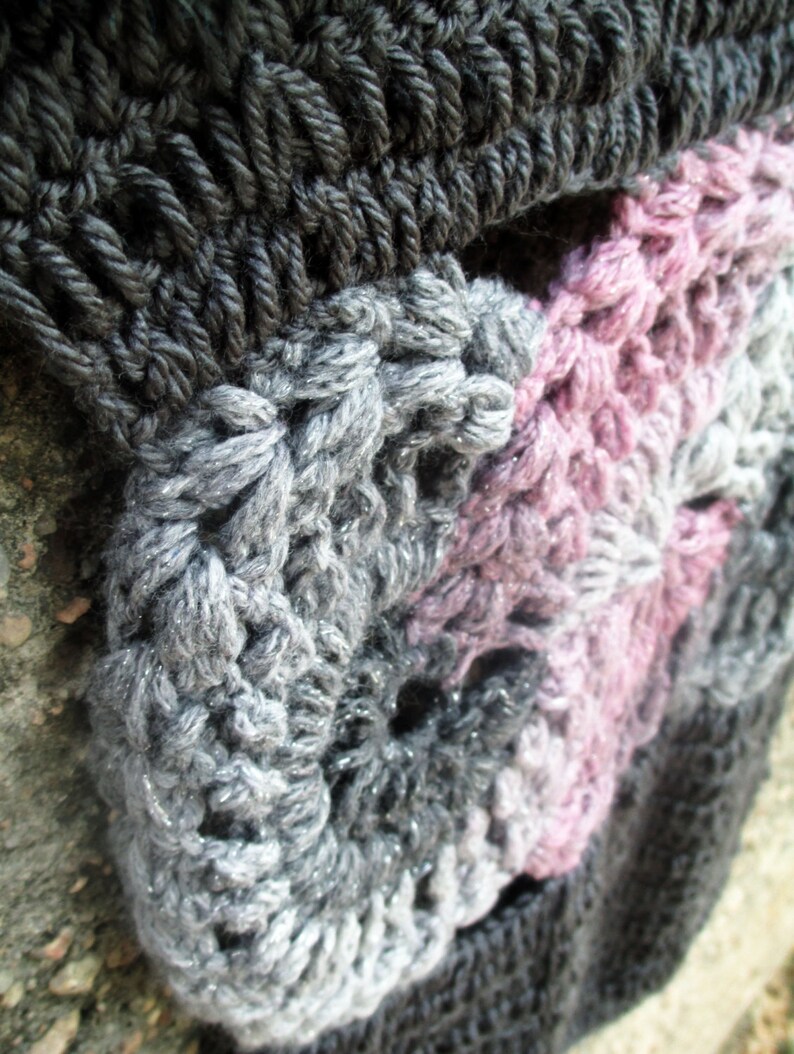 Op de afbeelding: Close-up van een gehaakte sjaal met een kleurverloop van zwart, grijs en roze. De sjaal is gemaakt van een dik garen en heeft een textuur met hobbels.