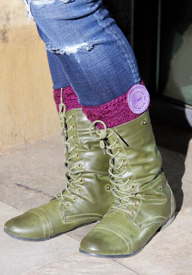 Puede incluir: Botas de combate de cuero verde con cordones y un pu&ntilde;o de punto morado. El pu&ntilde;o tiene un emblema redondo morado y plateado.