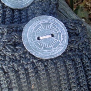 Puede incluir: Una tela de punto gris oscuro con un bot&oacute;n grande, redondo, en forma de br&uacute;jula. El bot&oacute;n tiene un anillo de metal plateado en el centro y est&aacute; marcado con n&uacute;meros y direcciones.