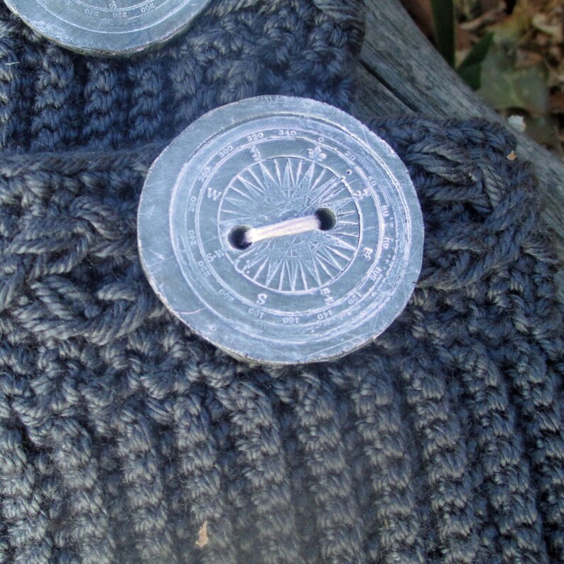 Puede incluir: Una tela de punto gris oscuro con un bot&oacute;n grande, redondo, en forma de br&uacute;jula. El bot&oacute;n tiene un anillo de metal plateado en el centro y est&aacute; marcado con n&uacute;meros y direcciones.