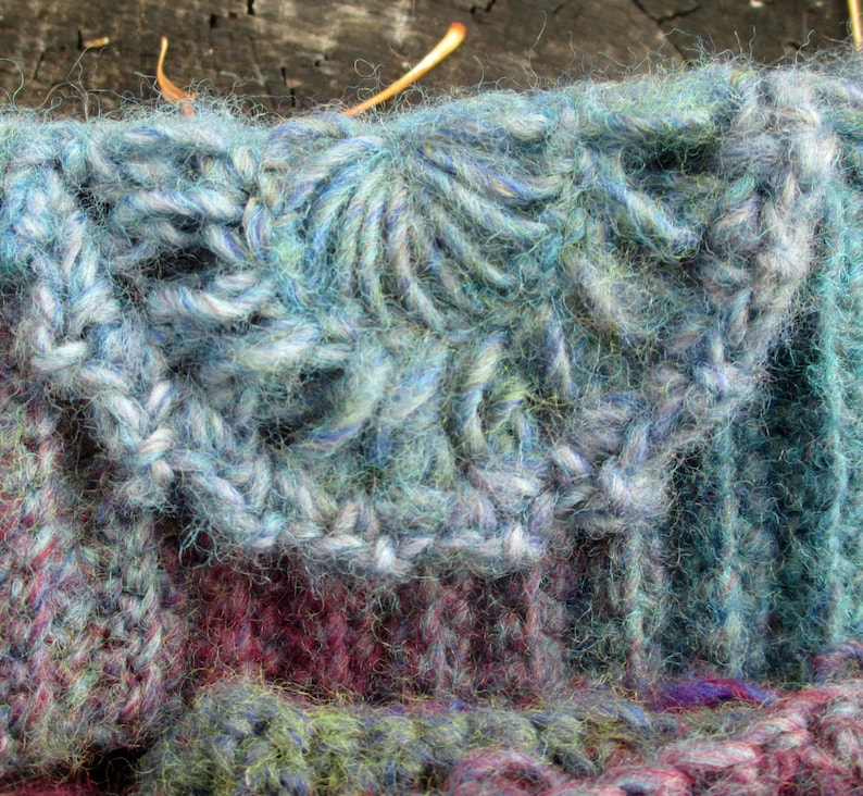 May include: Close-up of a knitted fabric with a blue and green color scheme. The fabric has a textured, fuzzy appearance and is made with a variety of yarn types.