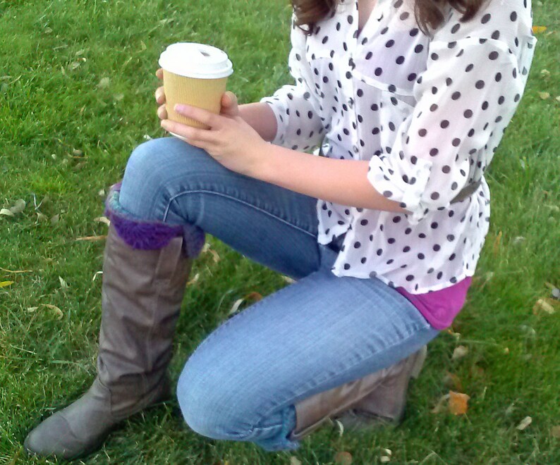 May include: A woman wearing blue jeans and a white polka dot shirt with brown boots. She is holding a brown paper cup.