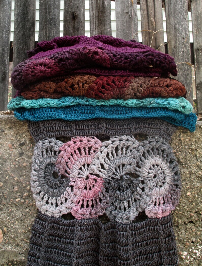 Op de afbeelding: Een gehaakt deken met een gelaagd ontwerp. De bovenste laag is donkerpaars, gevolgd door een bruine laag, een turquoise laag en een grijze laag. De onderste laag is een grijs en roze gehaakt ontwerp met een cirkelvormig patroon.