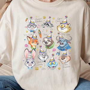 Puede incluir: Camiseta beige con ilustraciones coloridas de personajes de pel&iacute;culas, cada uno con un gorro de fiesta. Los personajes incluyen una oveja, un mapache, un guepardo, un zorro, un perezoso, un b&uacute;falo, un conejo, un gato y otros. El texto incluye nombres y frases.