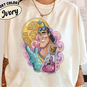 May include: Ivory-colored t-shirt featuring a cartoon illustration of a smiling character holding a gold coin and a potion bottle. The shirt has the words "Comfort Colors" and "Ivory" printed on it. The graphic is in shades of blue, yellow, pink, and purple.