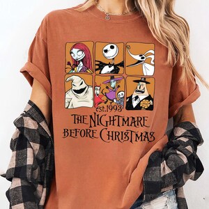 May include: Rust-colored t-shirt featuring a grid of six character portraits from "The Nightmare Before Christmas." The shirt includes the text "est. 1993" and "THE NIGHTMARE BEFORE CHRISTMAS" in black lettering.