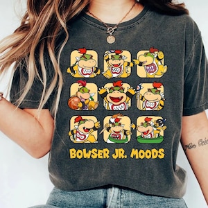 May include: Dark gray t-shirt featuring a grid of Bowser Jr. character illustrations in various moods. Each character is in a yellow square. The text "BOWSER JR. MOODS" is printed in yellow below the grid.