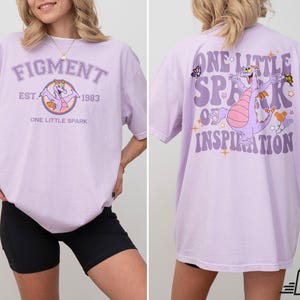 Op de afbeelding: Paars T-shirt met een cartoon-draak en de tekst "Figment Est. 1983 One Little Spark" op de voorkant en "One Little Spark of Inspiration" op de achterkant.