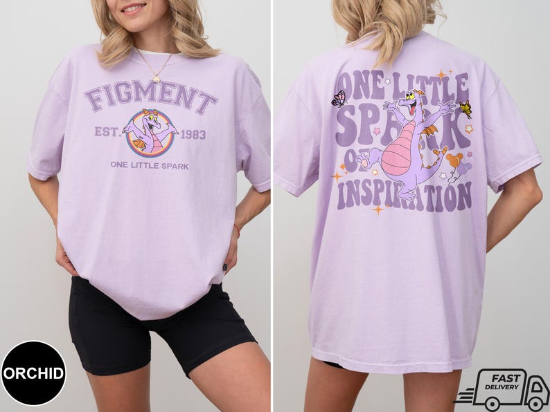 Op de afbeelding: Paars T-shirt met een cartoon-draak en de tekst "Figment Est. 1983 One Little Spark" op de voorkant en "One Little Spark of Inspiration" op de achterkant.