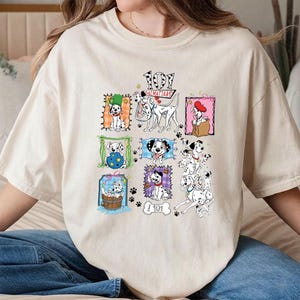 May include: Cream-colored t-shirt featuring a colorful graphic of various Dalmatian dog illustrations. The design includes the text "101 Dalmatians" and paw prints. The shirt is a casual, comfortable style.