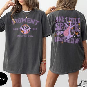 Op de afbeelding: Een oversized T-shirt in donkergrijs met een paarse draak afbeelding en de tekst "Pigment Est. 1983 One Little Spark" op de voorkant en "One Little Spark of Inspiration" op de achterkant.