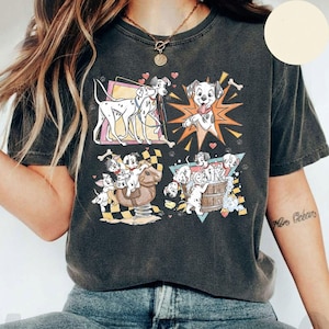 May include: Dark gray t-shirt featuring a graphic of Dalmatian dogs in various playful scenes. The design includes images of the dogs with bones, on a rocking horse, and in a wooden barrel. The shirt has a vintage, worn look.