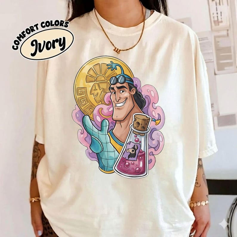 May include: Ivory-colored t-shirt featuring a cartoon illustration of a smiling character holding a gold coin and a potion bottle. The shirt has the words "Comfort Colors" and "Ivory" printed on it. The graphic is in shades of blue, yellow, pink, and purple.