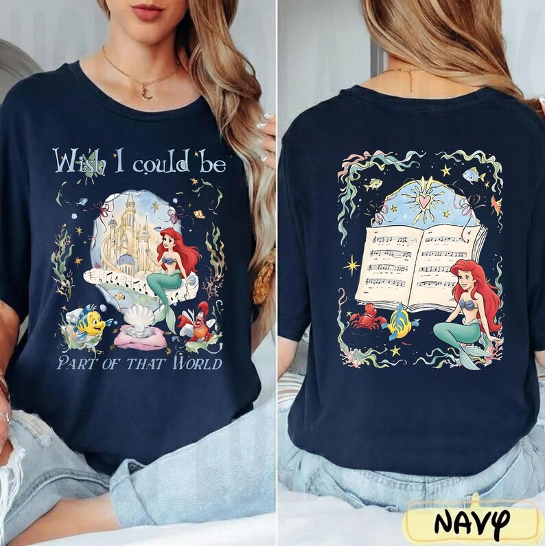 May include: Navy blue t-shirt featuring a colorful graphic of Ariel from The Little Mermaid. The front design includes Ariel, a castle, and the text "Wish I could be Part of That World." The back shows Ariel with a musical score.
