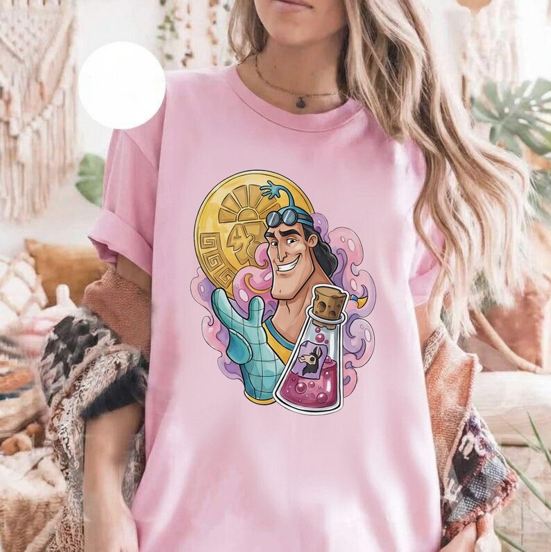 May include: Pink t-shirt featuring a cartoon character with a gold coin, a potion bottle, and a blue glove. The character has black hair and goggles. The potion bottle contains a purple liquid and a small figure.