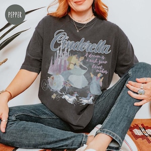 May include: A black t-shirt featuring a graphic print of Cinderella and Prince Charming. The text "Cinderella" is in a large, stylised font. The text "A dream is a wish your heart makes" is printed below the graphic.