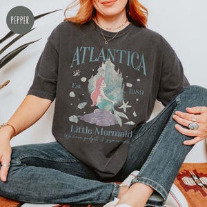 May include: A black t-shirt with a graphic print of Ariel from The Little Mermaid. The graphic includes the text "Atlantica Est. 1989" and "Little Mermaid".