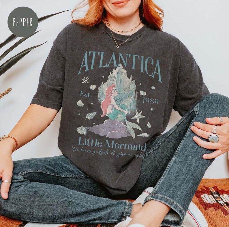May include: A black t-shirt with a graphic print of Ariel from The Little Mermaid. The graphic includes the text "Atlantica Est. 1989" and "Little Mermaid".