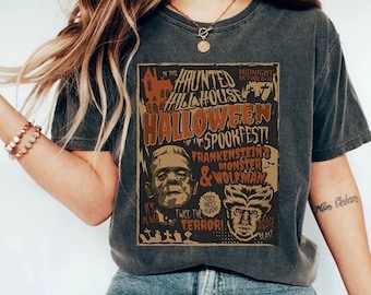 May include: Dark gray t-shirt featuring a vintage Halloween Spookfest design. The graphic includes Frankenstein's Monster and the Wolfman, with text that reads "Haunted Hill House" and "Twice the Terror!" A classic spooky tee.