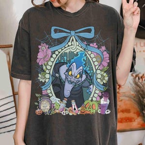 Pu&ograve; includere: T-shirt grigio scuro con un'illustrazione a cartoni animati di Ade di Hercules della Disney. Il design include Ade con fiamme blu, fiori, un fiocco blu e il testo "Deadly Night Shade".