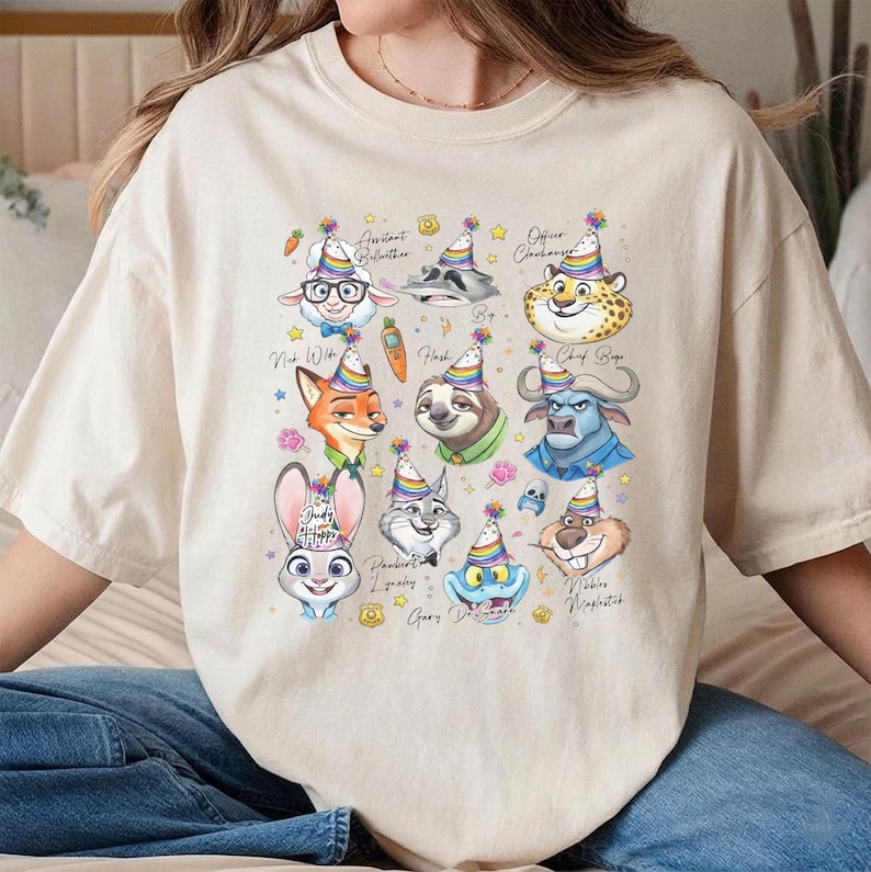 Puede incluir: Camiseta beige con ilustraciones coloridas de personajes de pel&iacute;culas, cada uno con un gorro de fiesta. Los personajes incluyen una oveja, un mapache, un guepardo, un zorro, un perezoso, un b&uacute;falo, un conejo, un gato y otros. El texto incluye nombres y frases.